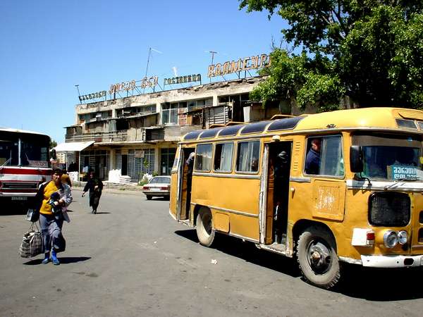 photo of Republic of Georgia, busstation of Gori, old Georgian yellow intercity bus with in the background the ex-soviet gastinjitse of Gori, probably the worst (and maybe also cheapest) hotel in Georgia