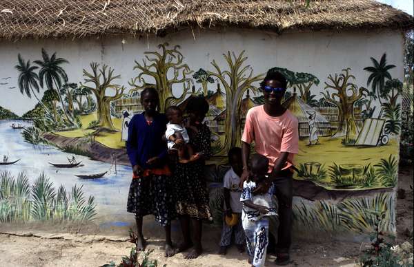 photo of Senegal, around Sine Saloum delta, local Senegalese village artist, proudly presenting the painting of the delta with baobabs and pirogues he painted on his house